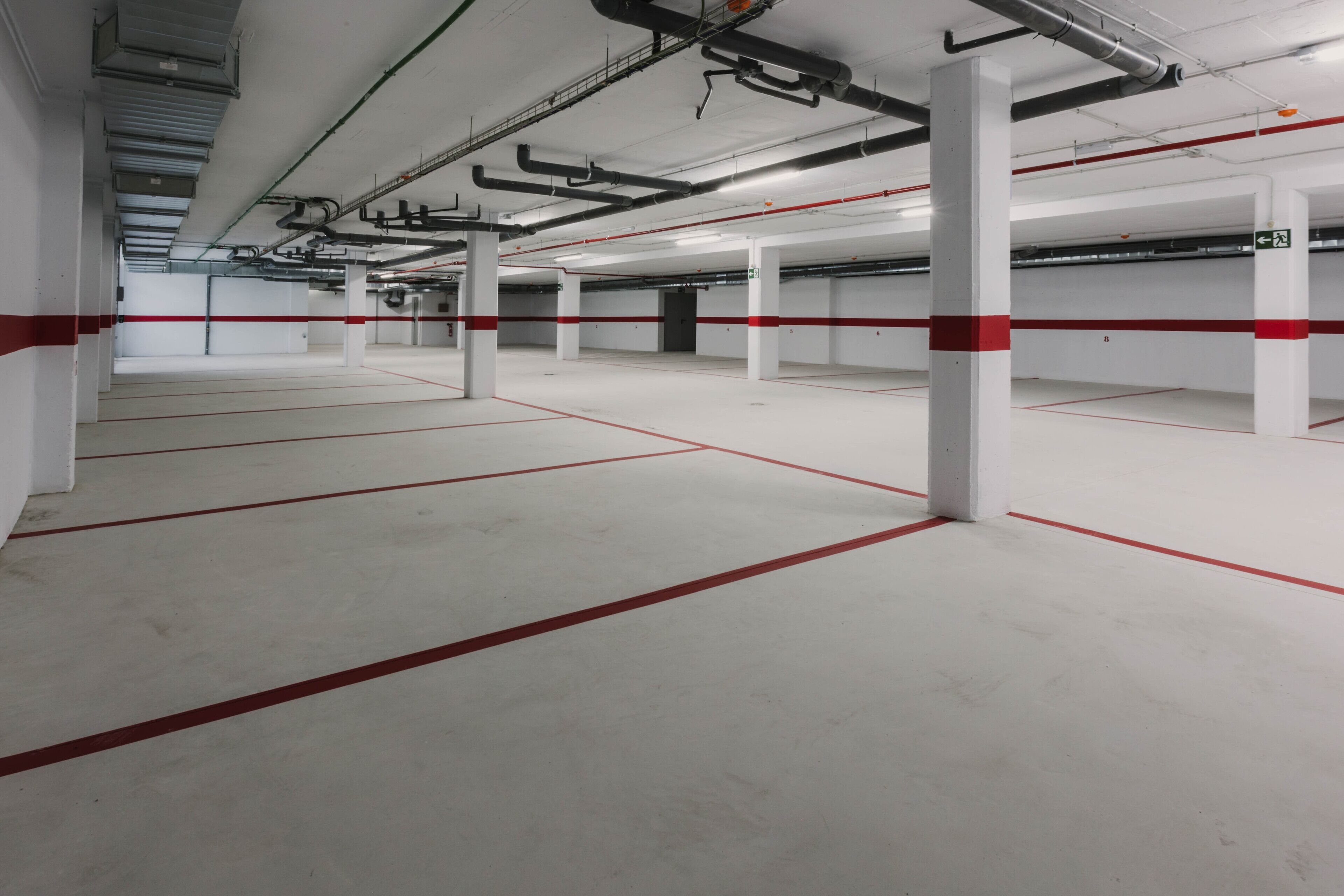 An indoor parking garage with white pillars and red lines marking parking spaces.