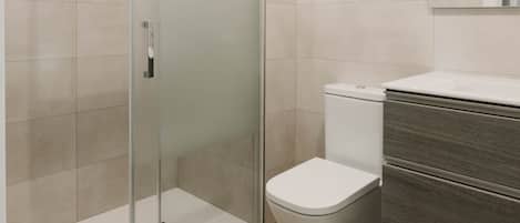 A modern bathroom with a glass-enclosed shower, a toilet, and a vanity with a mirror.