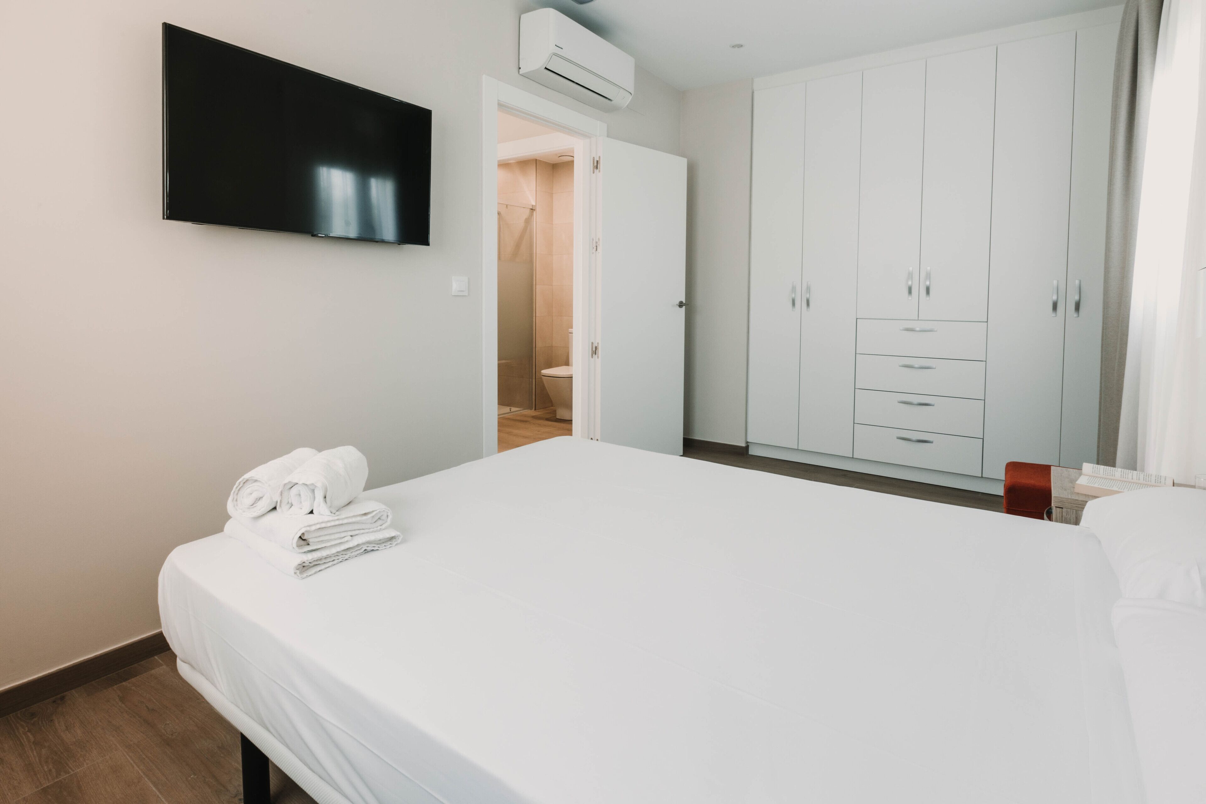 Habitación de hotel con cama, televisor montado en la pared, armario y unidad de aire acondicionado.