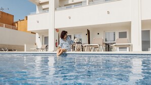 A poolside area with a person sitting by the pool, a dog, and a building with balconies and outdoor furniture. - Apartamentos SubUp (Cartagena)