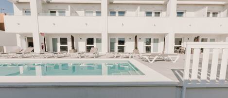 A modern building with a pool and sun loungers.