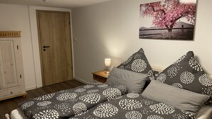 Quarto com cama, almofadas, mesa de cabeceira, luminária, porta e uma parede com uma pintura.