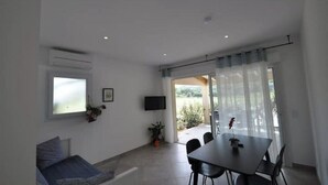 Ein modernes Wohnzimmer mit einer Couch, einem Esstisch mit Stühlen, einem an der Wand befestigten Fernseher und einer Glastür zum Außenbereich.