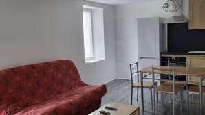 Un espace de vie moderne comprenant un canapé rouge, une table basse en bois, un coin repas avec des chaises en métal et une cuisine équipée d’une cuisinière et de placards.
