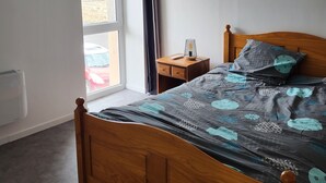 Une chambre à coucher avec un lit en bois, une table de chevet avec une lampe, une fenêtre avec des rideaux et une vue sur l’extérieur.
