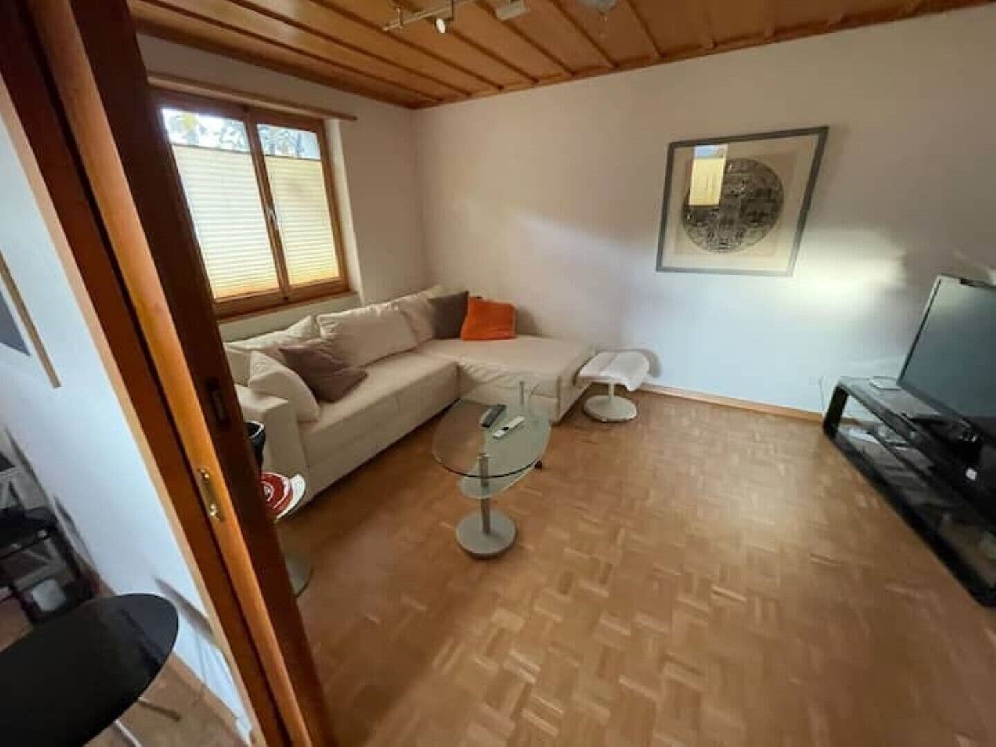 Olohuone, jossa on puinen katto, sohva, lasinen sohvapöytä, televisio ja seinällä oleva kehystetty taulu.