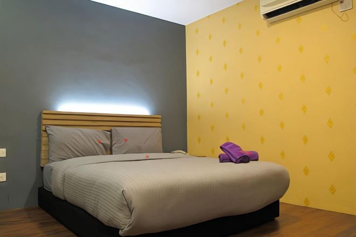 A single bed with a wooden headboard, a grey mattress, and a purple towel on the footboard.