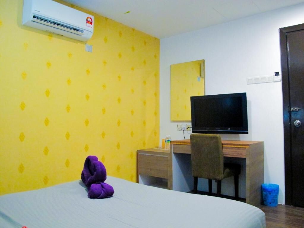 Quarto de hotel com cama, escrivaninha com cadeira, televisão e ar-condicionado.