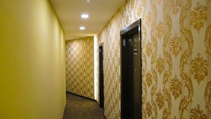 Um corredor com papel de parede estampado e chão coberto por carpete, que leva a duas portas e um elevador.