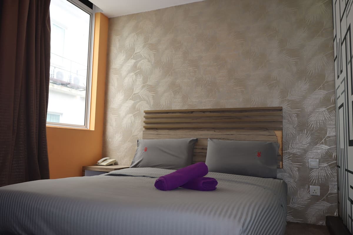 A hotel room with a bed, a nightstand, a telephone, and a window with curtains.