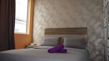 Una habitación de hotel con una cama, una mesita de noche, un teléfono y una ventana con cortinas.