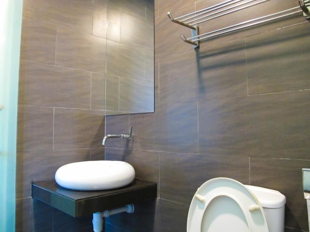 Casa de banho moderna com azulejos escuros, uma sanita e uma pia branca.