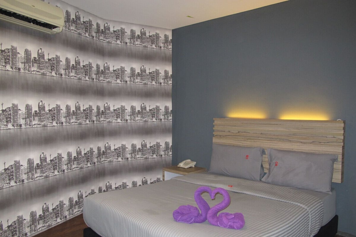 A hotel room with a bed, a nightstand, a telephone, and a headboard with a light.