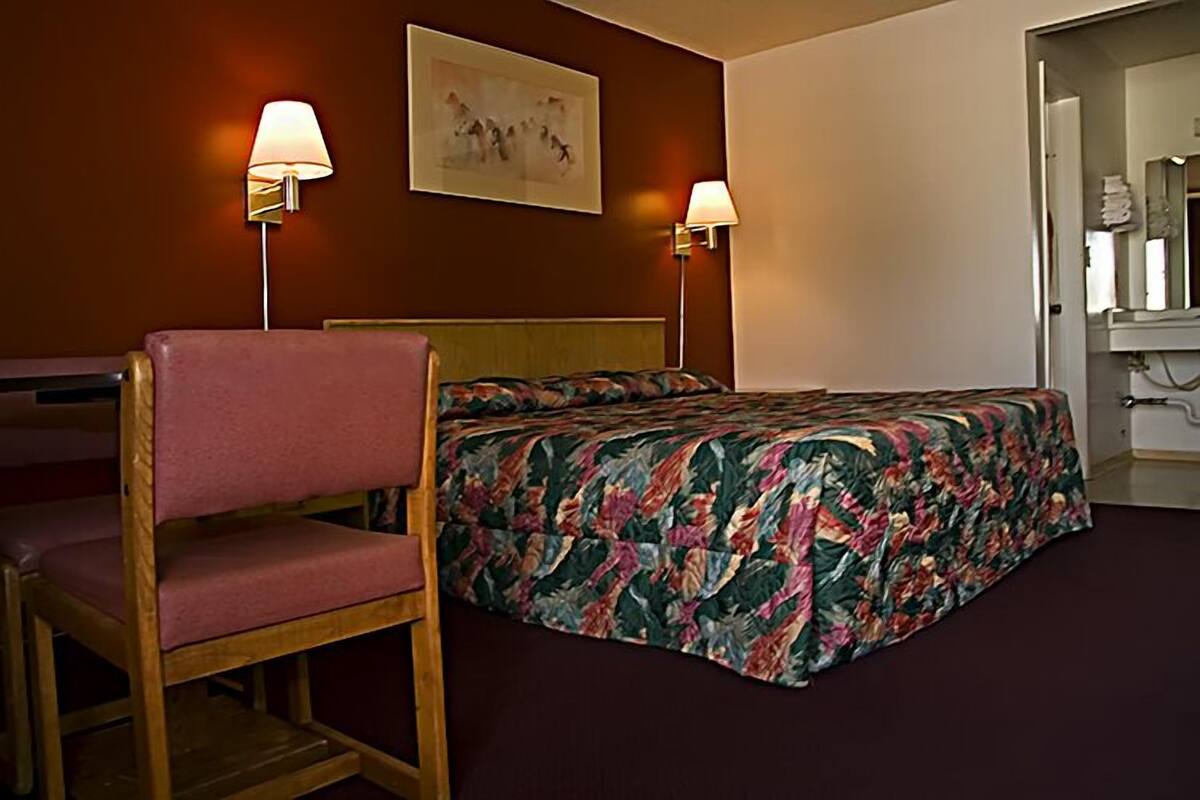 Una habitación de hotel con una cama, una silla, dos lámparas de pared y un cuadro en la pared.