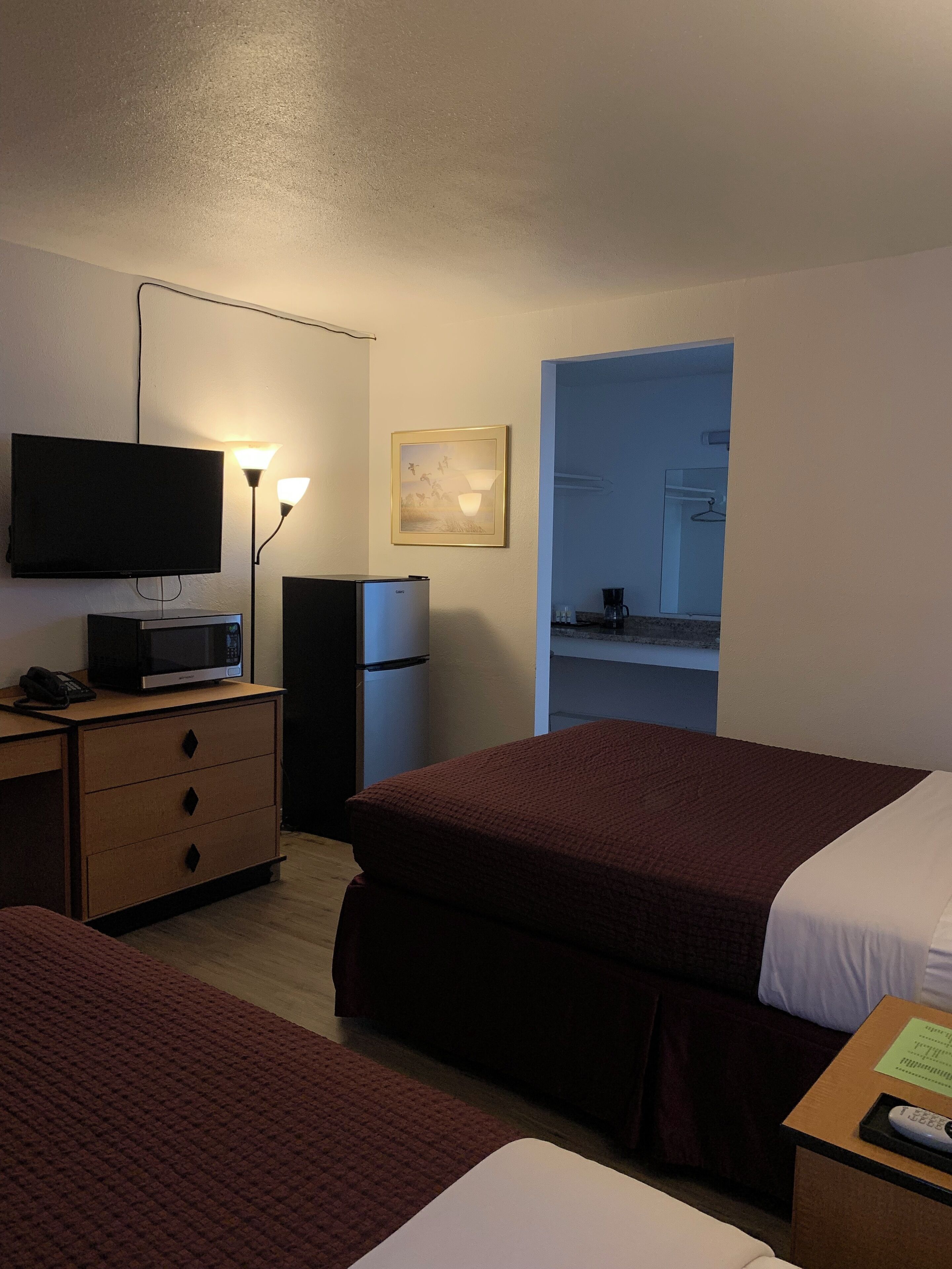Habitación de hotel con dos camas, televisión, refrigerador, microondas, escritorio con cajones y una pequeña cocina americana.