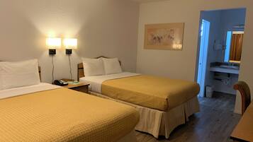 A hotel room with two beds, a nightstand, a painting, and a bathroom visible through an open door.