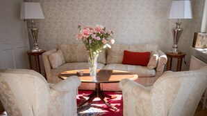 Un salon comprenant un canapé, deux fauteuils, une table basse et un vase de fleurs. Deux lampes sont placées de part et d’autre du canapé.