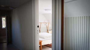 Une pièce avec un lit, une chaise en bois et une fenêtre.