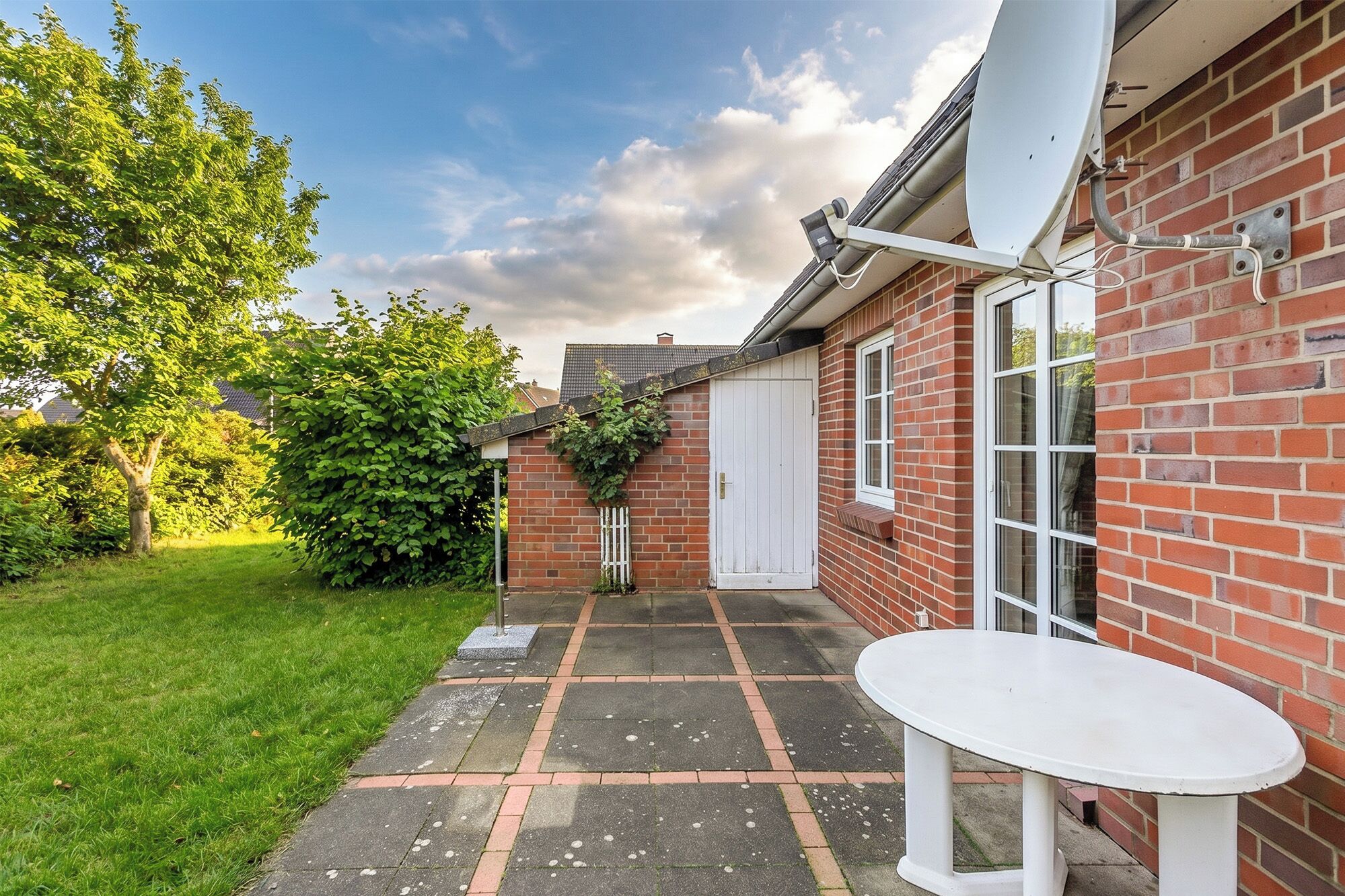 A brick house with a white door, a satellite dish, and a small patio with a table.