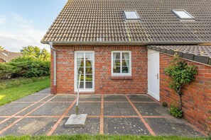 A brick house with a tiled roof, two windows, a door, and a small garden area.