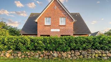 Een tweelaags huis met een bakstenen gevel, twee ramen met witte omlijstingen, en een stenen muur ervoor.
