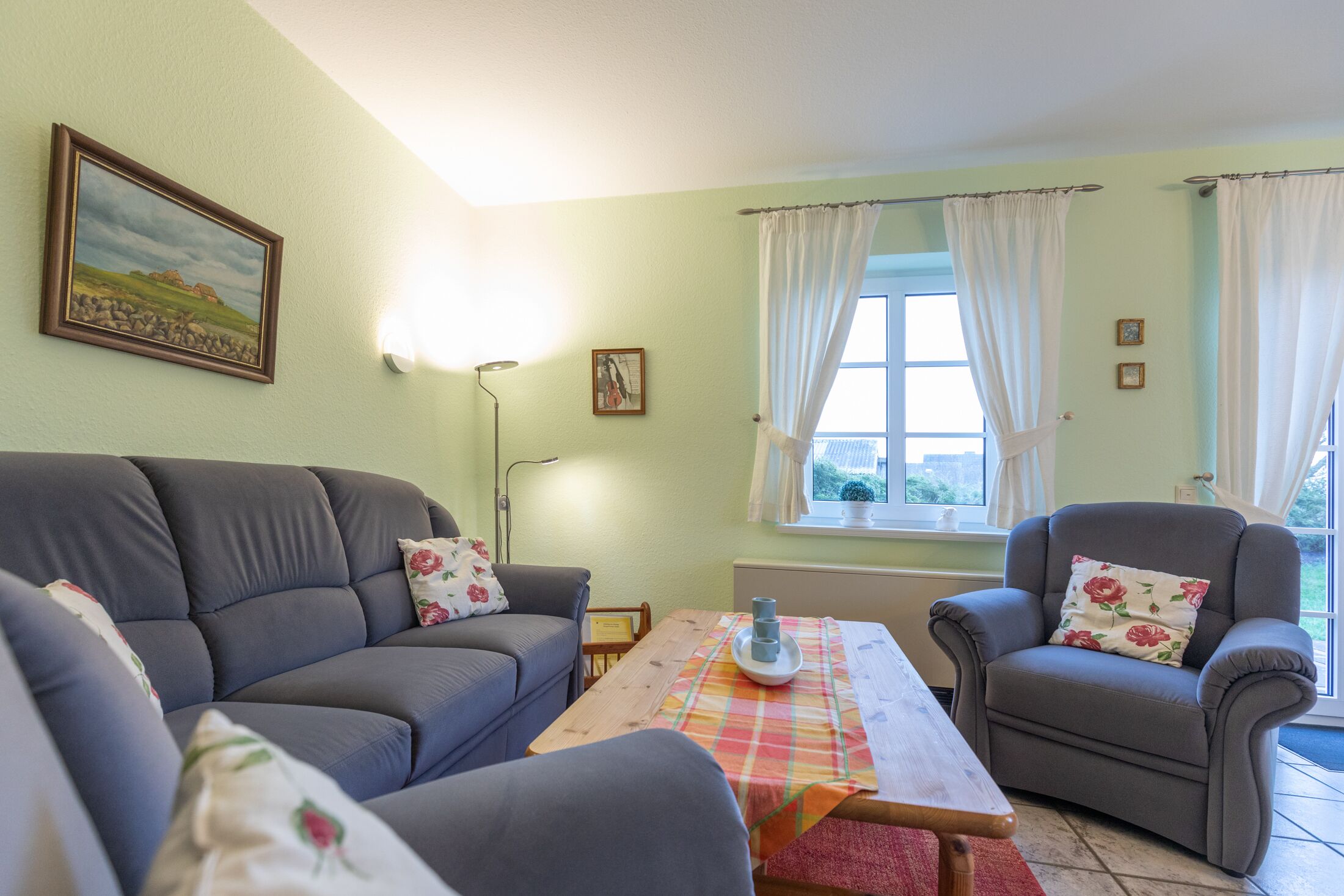Una sala de estar con sofá, sillón y una mesa con mantel individual.
