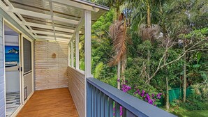 A wooden deck with a pergola, surrounded by lush greenery and purple flowers. - Marine Villa @ Smiths Lake (Tarbuck Bay)