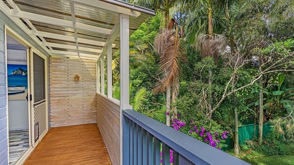 A wooden deck with a pergola, surrounded by lush greenery and purple flowers.