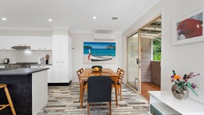 A modern kitchen with white cabinets, a dining area with a wooden table and chairs, and a large window with a view of greenery. - Marine Villa @ Smiths Lake (Tarbuck Bay)