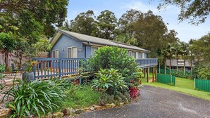 A two-story house with a blue exterior, a covered porch, and a garden with various plants and a pathway leading to the entrance. - Marine Villa @ Smiths Lake (Tarbuck Bay)