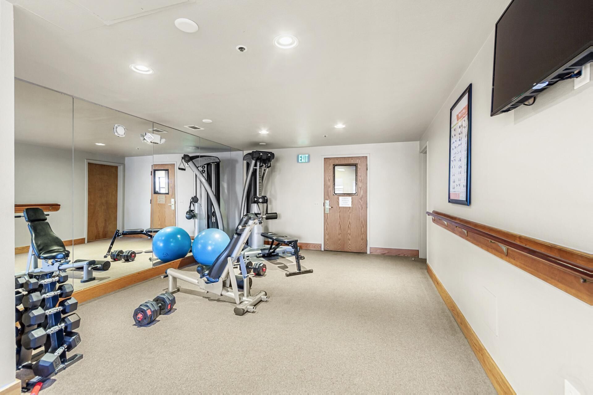 Une salle de sport équipée de matériel d’exercice, avec un miroir et un téléviseur accroché au mur.