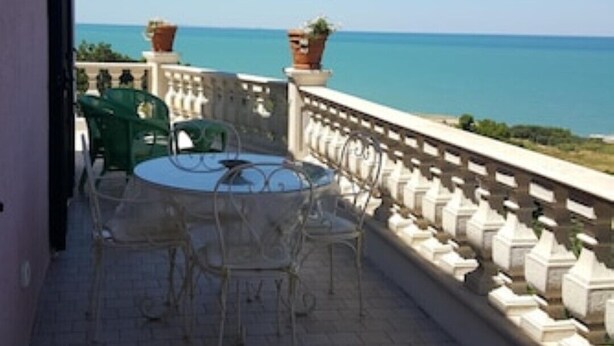 Ein Balkon mit Tisch und Stühlen, mit Blick auf ein Gewässer.