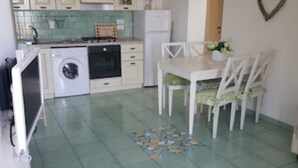 Eine kleine Küche mit Waschmaschine, Herd und Esstisch mit Stühlen.