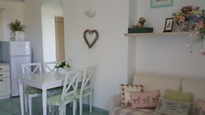 Ein Essbereich mit weißem Tisch und Stühlen, einer herzförmigen Dekoration an der Wand und einer Couch mit gemusterten Kissen.
