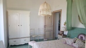 Ein Schlafzimmer mit einem großen weißen Kleiderschrank, einem Nachttisch mit Lampe und einem Bett mit gemustertem Überwurf.