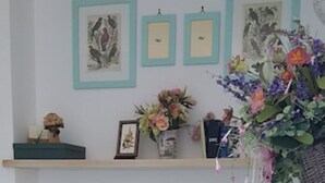 Ein Wohnzimmer mit einem Karo-Sofa, einem Couchtisch mit Blumenvase und einem Regal mit gerahmten Bildern und einer kleinen Pflanze.