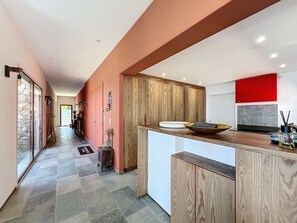 A modern kitchen with wooden cabinets, a red accent wall, and a large island with a bowl and book.