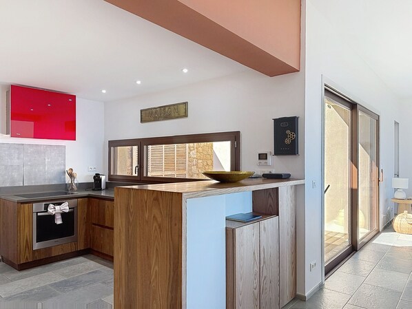 A modern kitchen with a central island, a built-in oven, and a red appliance on the wall. - Stunning villa, sunset ocean view, heated pool, 4 bedrooms (Corbara)
