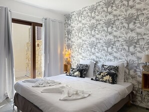 A hotel room with a bed, two pillows, a nightstand, a lamp, and a view of a building through a glass door.
