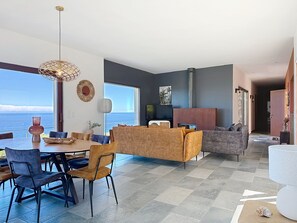Una sala moderna con comedor, ventanas amplias y vista al mar.