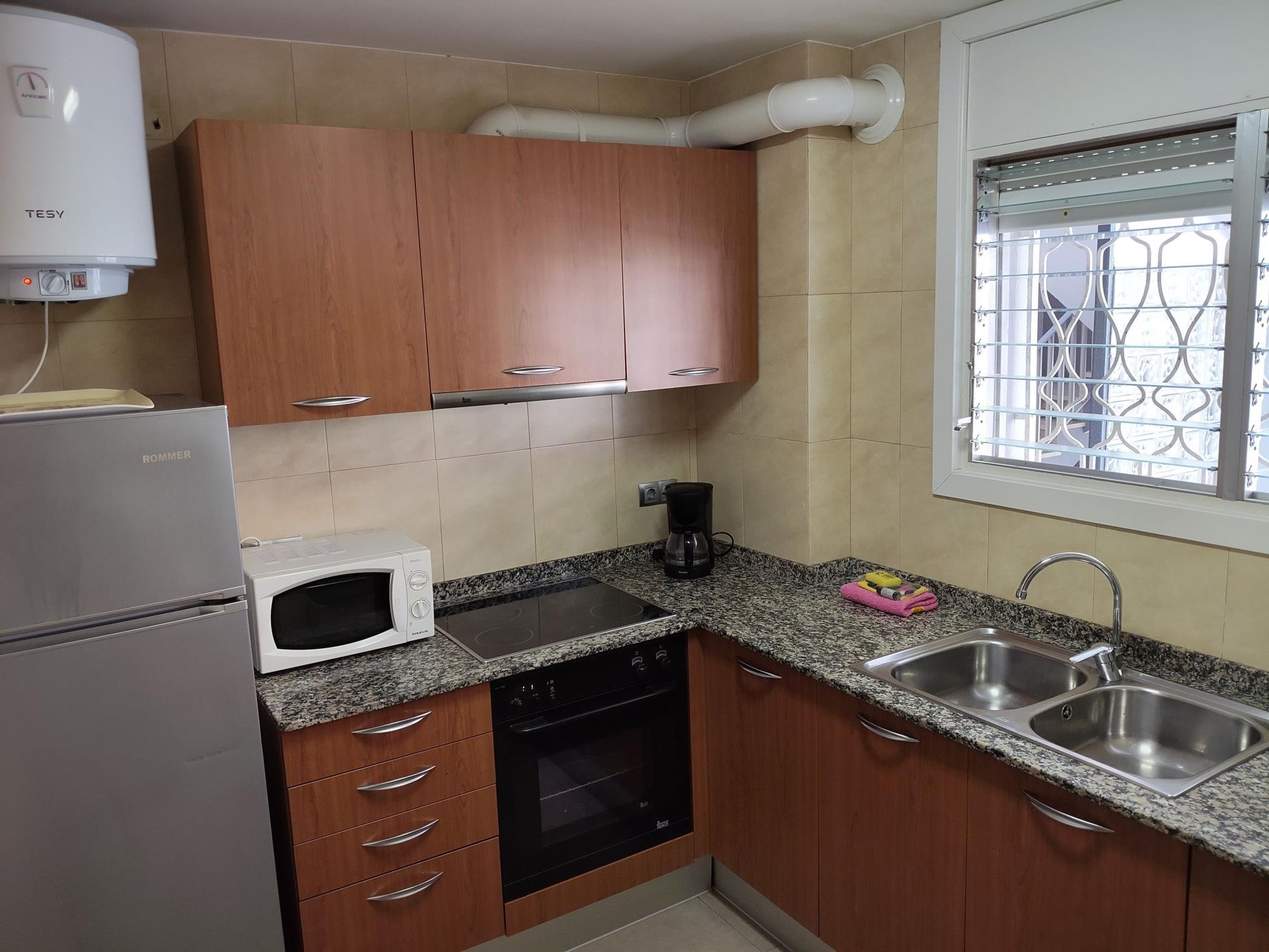 A compact kitchen with wooden cabinets, a built-in oven, a microwave, and a sink.