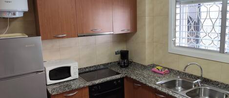 A compact kitchen with wooden cabinets, a built-in oven, a microwave, and a sink.