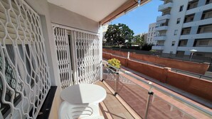 A balcony with a white plastic table and chairs, a metal railing, and a view of a cityscape with buildings and a clear sky.