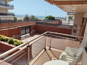 Un balcón con vista a la playa, piso de baldosas y una silla blanca de plástico.