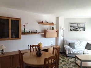Una habitación con una mesa de comedor, sillas, un sofá, un armario y una estantería de pared con objetos decorativos.