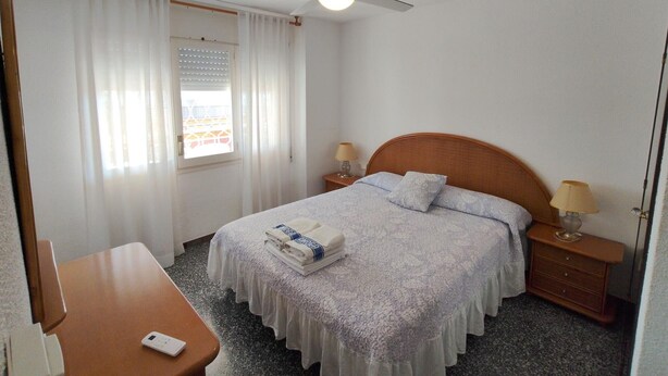 A hotel room with a bed, two bedside tables, a ceiling fan, a window with curtains, and a small table.