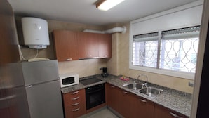 A compact kitchen with a refrigerator, microwave, dishwasher, and a window with decorative bars.