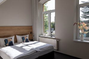 A bedroom with a bed, a window, a radiator, and a vase with flowers. - Gästehaus am Lausitzring (Sallgast)