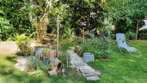 Een tuin met een houten bankje, een metalen stoel en diverse planten.