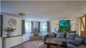 Een woonkamer met een bank, een salontafel, een klok en een schilderij aan de muur.